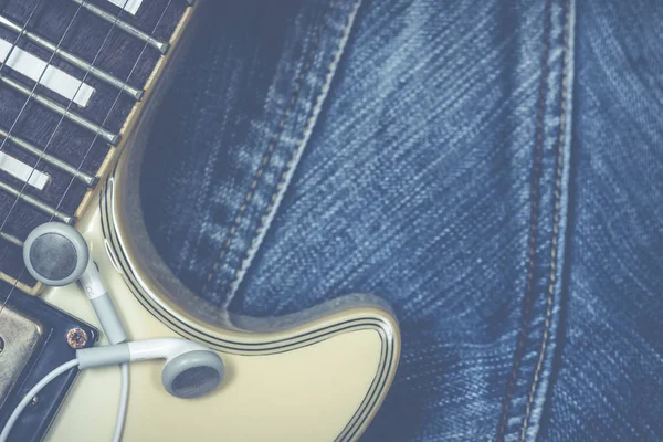 white earphones & electric guitar fingerboard on blue denim jeans