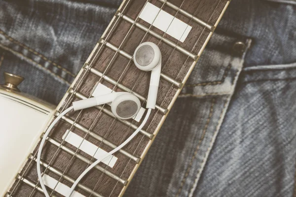 white earphones & electric guitar fingerboard on blue denim jeans