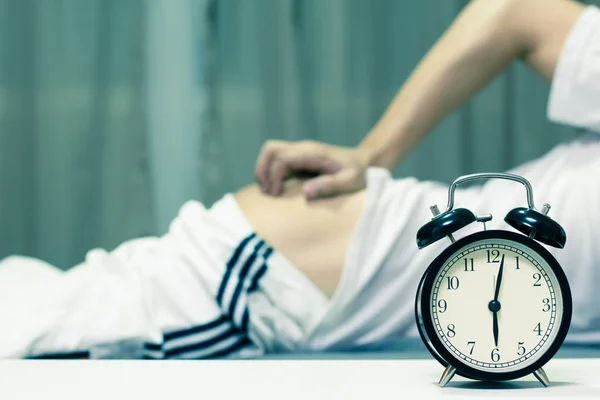 Schlafender asiatischer junger Mann vom Wecker am frühen Morgen auf dem Bett gestört & am Arsch gekratzt — Stockfoto