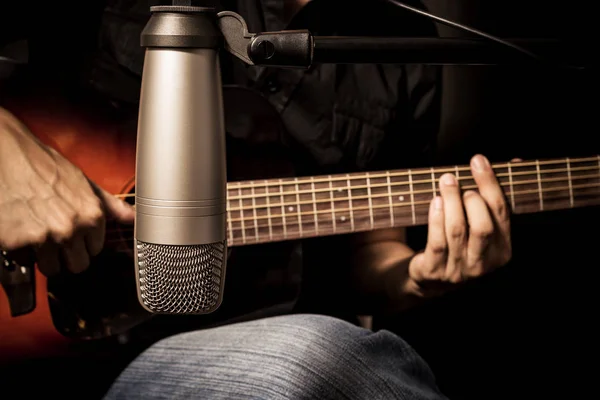 Musicien masculin jouant de la guitare acoustique derrière le microphone à condensateur en studio d'enregistrement — Photo