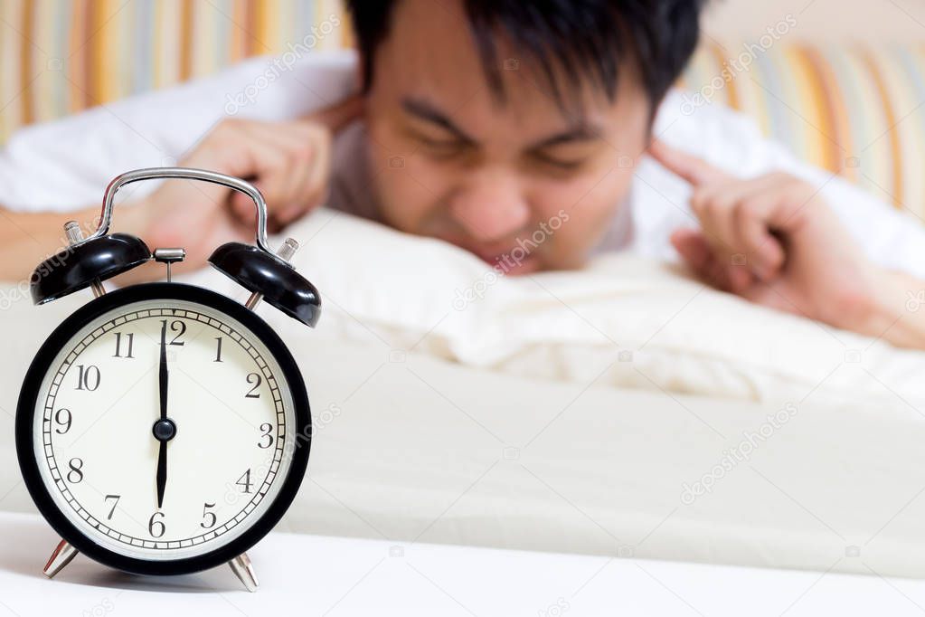 sleeping asian young male disturbed by alarm clock early morning on bed