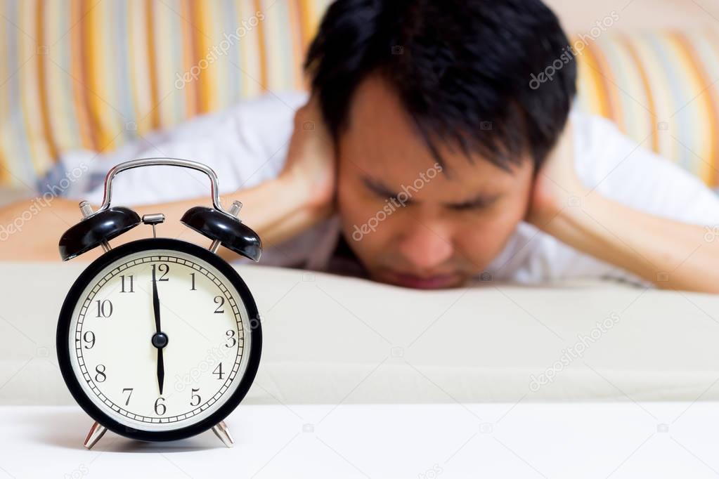 sleeping asian young male disturbed by alarm clock early morning on bed