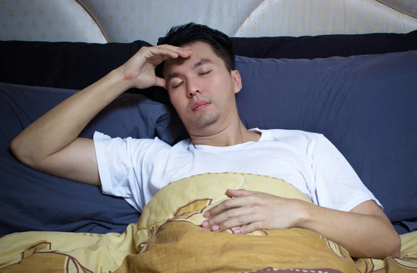 Азіатський чоловік в ліжку страждає безсонням, головним болем і розладом сну думаючи про свою проблему — стокове фото