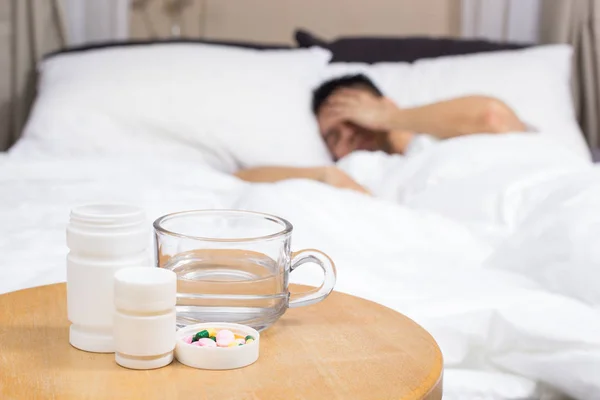 Asiatischer Mann auf weißem Bett mit Tabletten, Medikamenten und Glas Wasser leidet unter Schlaflosigkeit, Kater, Kopfschmerzen in der Nacht — Stockfoto