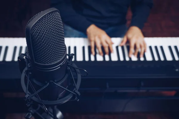 ไมโครโฟนคอนเดนเซอร์บนมือของนักดนตรีชายเล่นเปียโนพื้นหลัง — ภาพถ่ายสต็อก