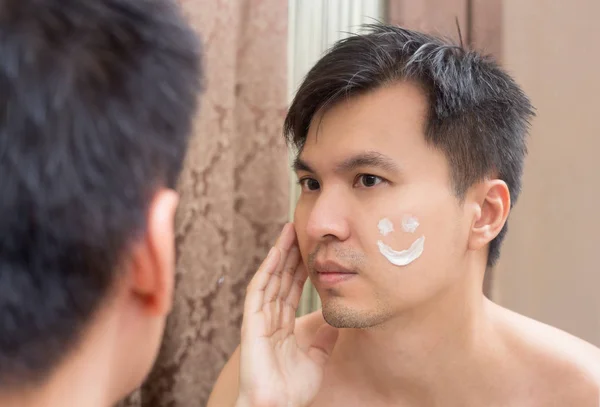 Miroir reflet d'un jeune asiatique beau homme appliquant faciale — Photo