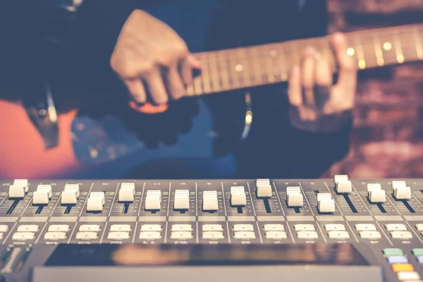 Чоловічий музикант грає на акустичній гітарі за звуковим мікшером у студії звукозапису, зосереджується на фейдері — стокове фото