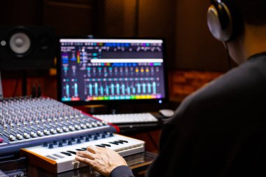 Asyalı erkek müzik yapımcısının ev kayıt stüdyosunda Midi klavyesinde ve bilgisayarda bir şarkı düzenlemesi. müzik üretim konsepti