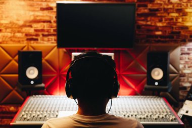 Kayıt stüdyosunda ses karıştırma konsolu üzerinde çalışan Asyalı erkek müzik yapımcısının arkası. müzik üretimi, yayıncılık, post prodüksiyon konsepti