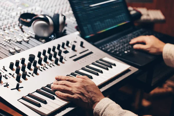 music producer hands composing a song on synthesizer keyboard and laptop computer in recording studio