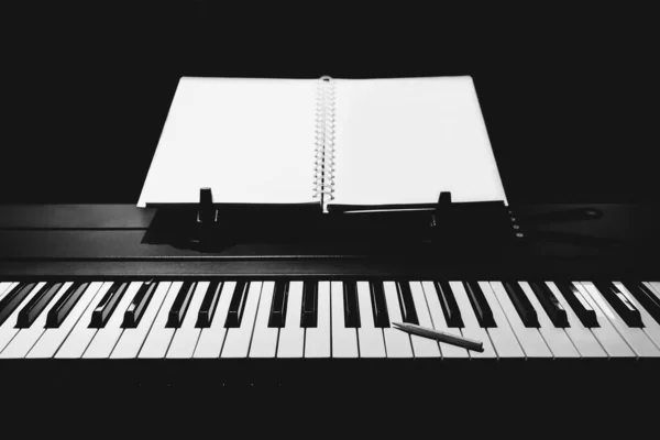 song writing concept. pencil on piano keys with blank white music sheet