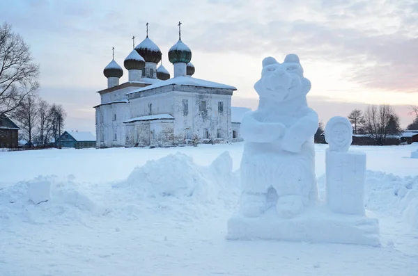 Russia, Arkhangelsk region. Kargopol, Ice sculpture of Masha and bear in front of Annunciation (Blagoveschenskaya) church in the winter evening on New square at sunset