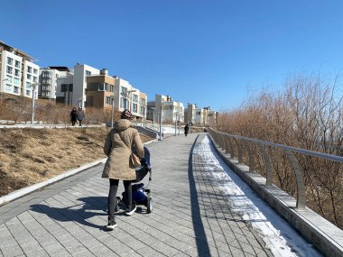 Vladivostok, Rusya, Mart, 13. 2020. İlkbaharın başlarında Patroclus (Patrokl) körfezinde gezinti güvertesi boyunca yürüyen bebek arabalı genç bir kadın. Vladivostok, Rusya