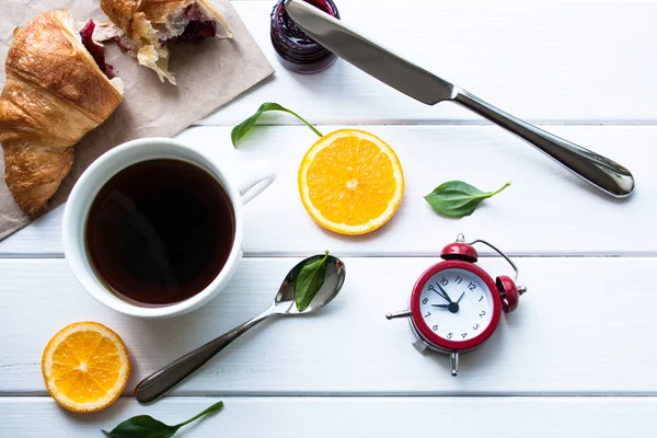 Croissants, koffie en wekker op een witte houten tafel — Stockfoto