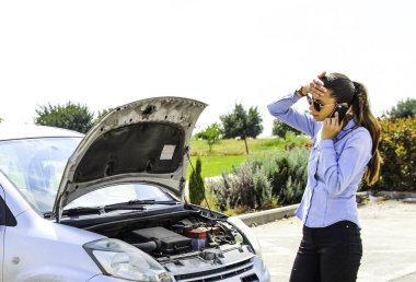 Kırık bir araba, bir kadınla telefonda konuşurken kafasını tutar ve yardım için bekler 