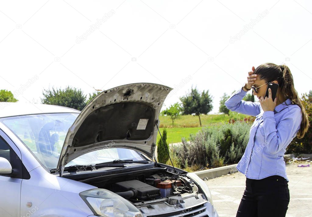 A woman with a broken car holds her head,talking on the phone waits for assistance