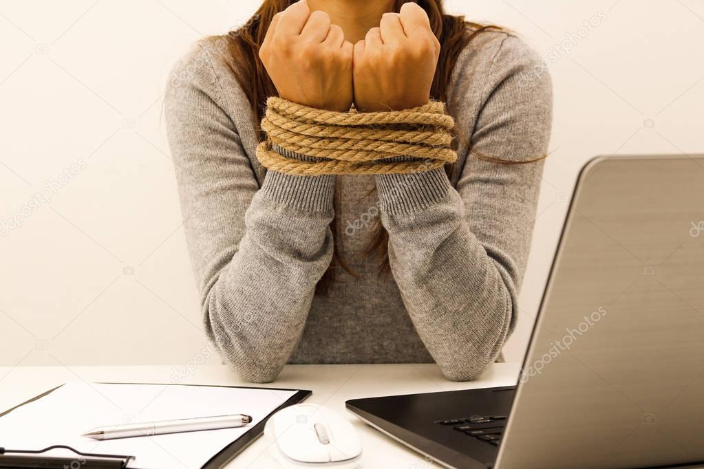 A woman with a laptop in the office with her hands tied with a rope