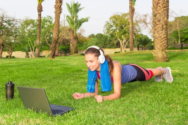 genç bir kız spor egzersizleri laptop ve kulaklık ile çimenlerin üzerinde bir parkta mı.