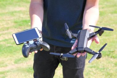 Uzaktan kumanda cep telefonu ile genç adam dron tutun. Güneşli yeşil