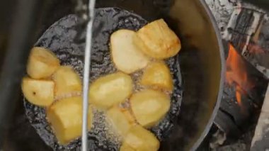 Ağır çekim. Açık ateşte kazanda yemek pişirmek. Yağda kızartılmış patateslerin yakın çekimi.