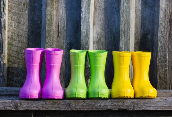 Multicolored rubber boots on a wooden background. Pink, green, and yellow boots stand in a row.