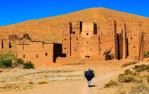 Mujer marroquí llevando una bolsa grande con hierbas con kasbah en el b — Foto de Stock