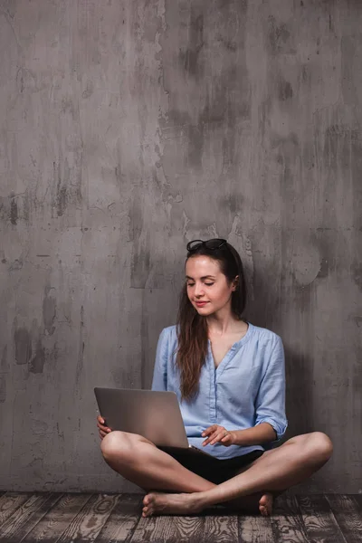 Młoda kobieta uśmiechający się, siedząc na podłodze drewnianej z laptopa — Zdjęcie stockowe