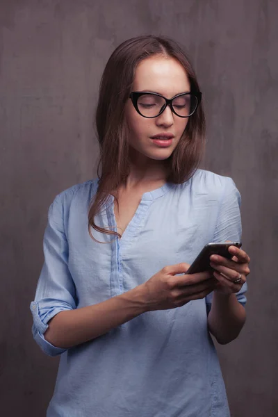 Lachende vrouw in glazen met behulp van mobiele telefoon — Stockfoto