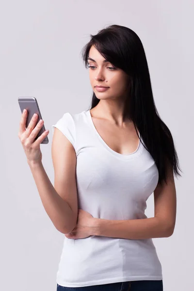 Молодая девушка держит мобильный телефон и смотрит в сторону — стоковое фото