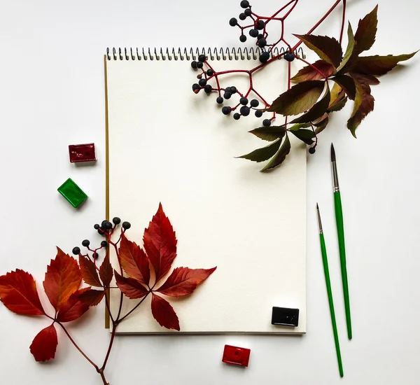 Composição de outono com álbum, aquarelas e pincéis, decorados com folhas vermelhas e bagas. Deitado plano, vista superior — Fotografia de Stock