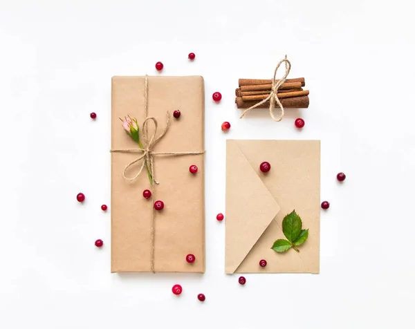 Подарункова коробка та конверт в екологічному папері на білому тлі. Подарунки прикрашені трояндами та ягодами. Концепція свята, вид зверху, плоский ліжко — стокове фото