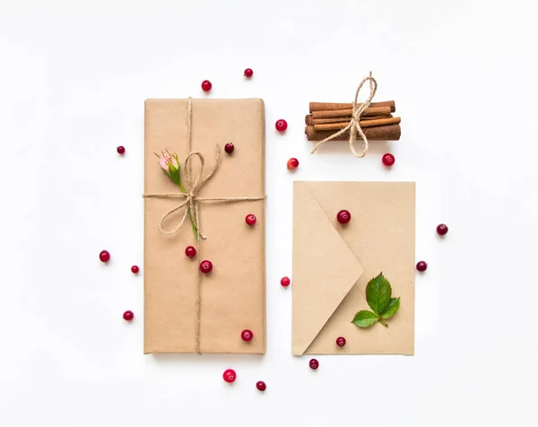 Caixa de presente e envelope em papel ecológico sobre fundo branco. Presentes decorados com rosas e bagas. Conceito de férias, vista superior, flat lay — Fotografia de Stock