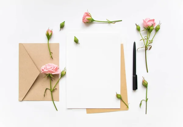 Brev och eco papper kuvert på vit bakgrund. Inbjudningskort, eller kärleksbrev med rosa rosor. Holiday koncept, ovanifrån, platt låg — Stockfoto