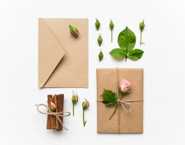 Presentförpackning och kuvert i eco papper på vit bakgrund. Presenterar dekorerad med rosor. Holiday koncept, ovanifrån, platt låg — Stockfoto