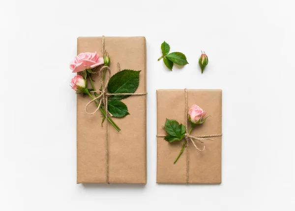 Cajas de regalo en papel ecológico sobre fondo blanco. Regalos decorados con rosas. Concepto de vacaciones, vista superior, plano —  Fotos de Stock