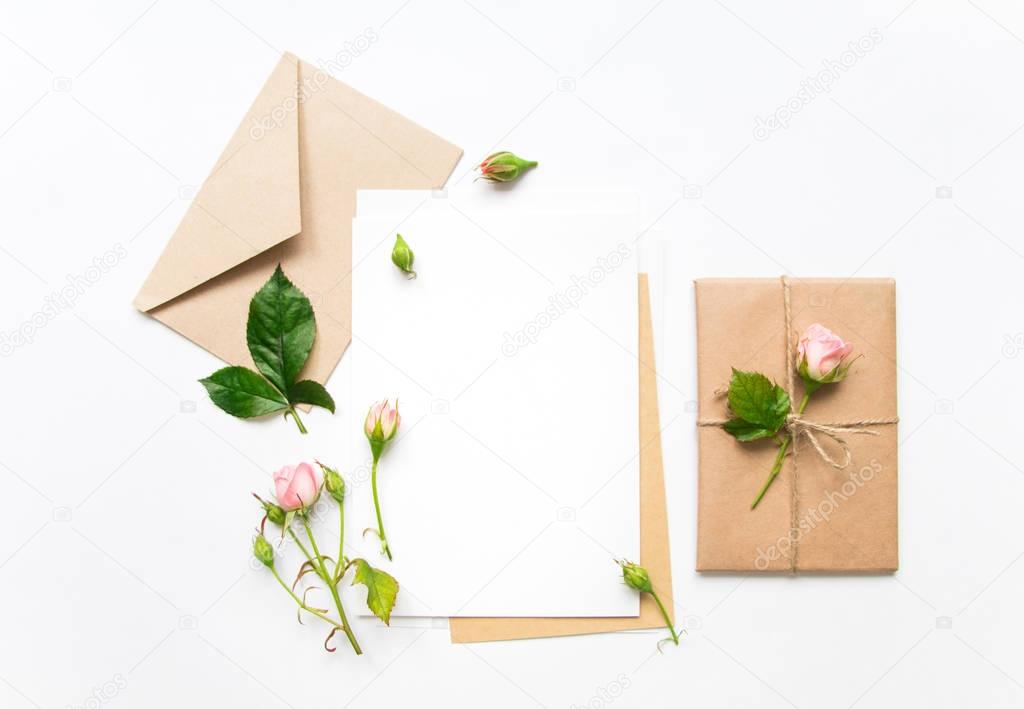 Letter, envelope and gift on white background. Invitation cards, or love letter with pink roses. Holiday concept, top view, flat lay