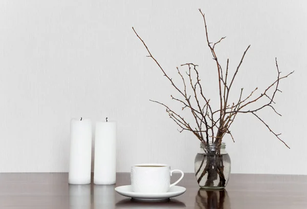 Tasse, Kerzen und Zweige in Flaschen auf einem Holztisch. romantisches grau-weißes Stillleben — Stockfoto