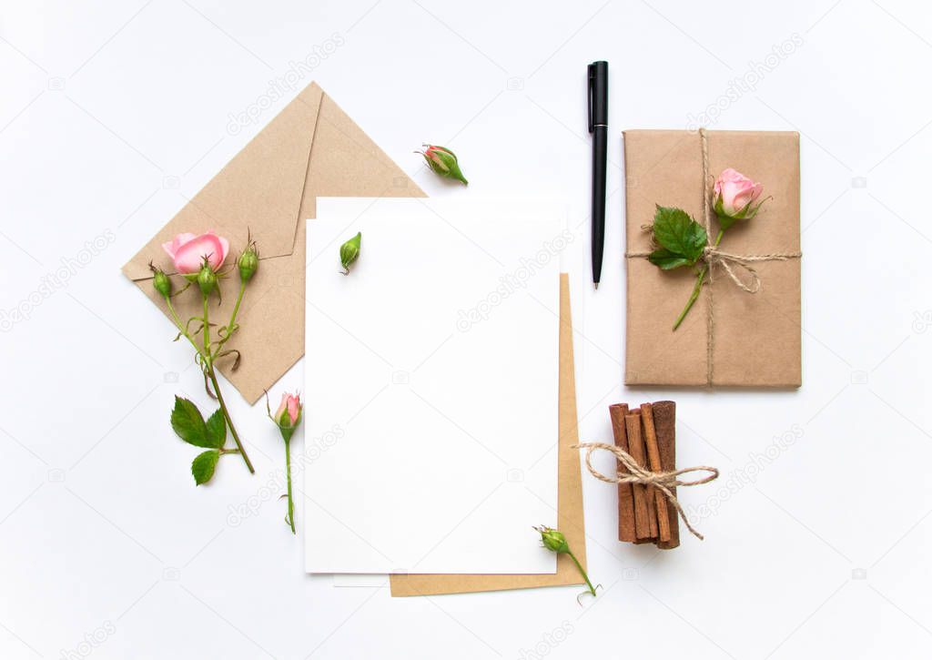 Letter, envelope and gift on white background. Invitation cards, or love letter with pink roses. Holiday concept, top view, flat lay