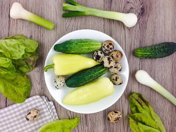 Colorful composition with vegetables and quail eggs on a plate on wooden background. Flat lay, top view — Stock Photo, Image