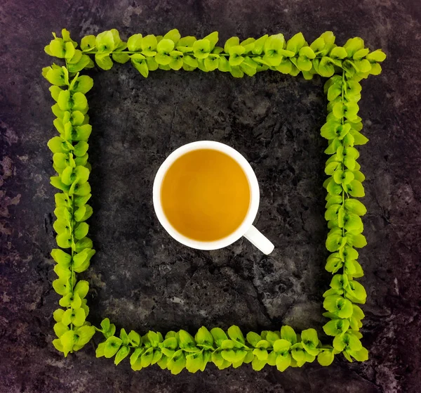 Taza de té en marco de ramas verdes sobre fondo de piedra oscura. Vista superior — Foto de Stock