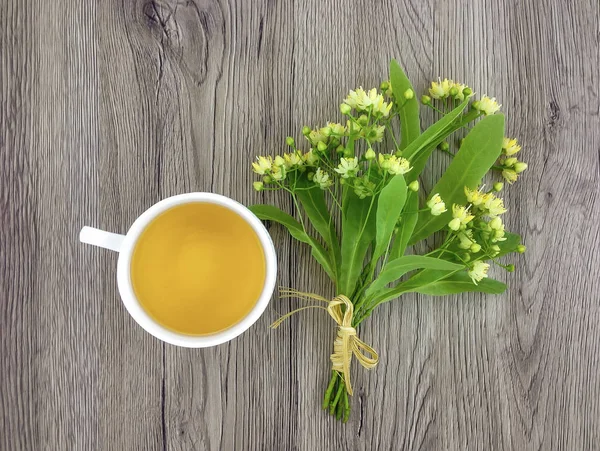 Lindo ramo de flores de tilo y taza de té en la mesa de madera. Piso tendido, vista superior —  Fotos de Stock