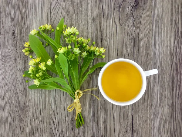 Lindo ramo de flores de tilo y taza de té en la mesa de madera. Piso tendido, vista superior — Foto de Stock