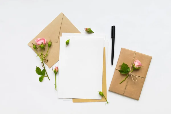 Carta, sobre y regalo sobre fondo blanco. Tarjetas de invitación, o carta de amor con rosas rosadas. Concepto de vacaciones, vista superior, plano —  Fotos de Stock