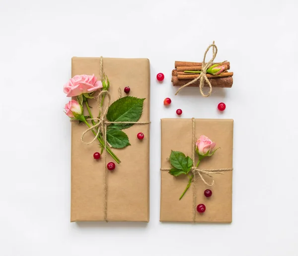 Gift box and envelope in eco paper on white background. Presents decorated with roses and berries. Holiday concept, top view, flat lay — Stock Photo, Image