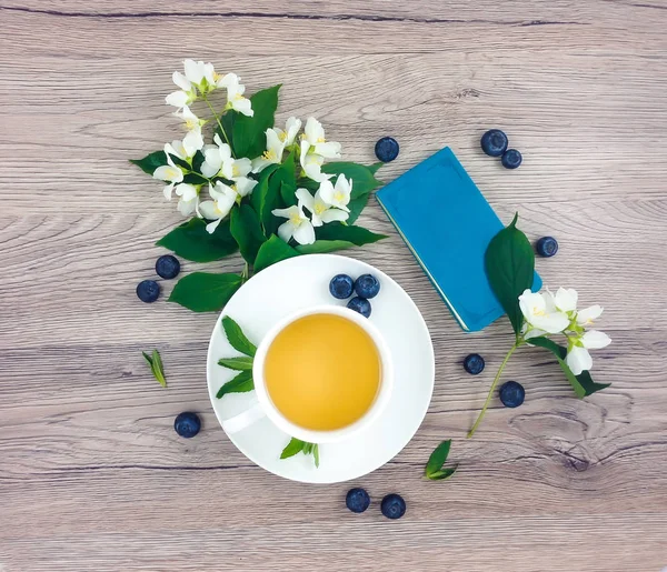Composición de primavera de la taza de té, cuaderno y flores en la mesa de madera, la puesta plana — Foto de Stock