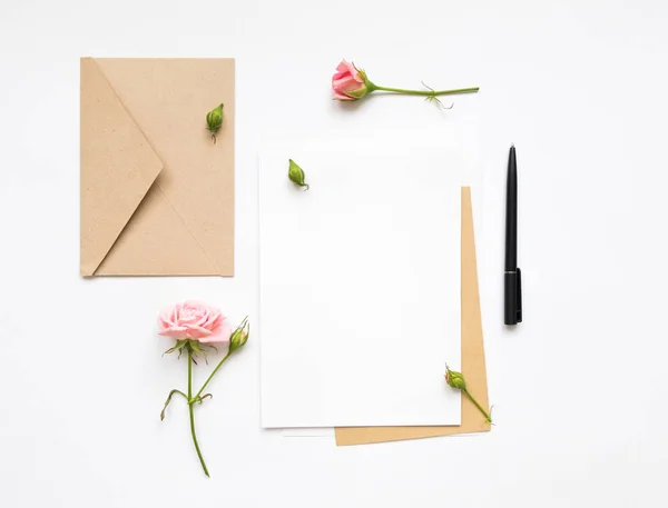 Brev och eco papper kuvert på vit bakgrund. Inbjudningskort, eller kärleksbrev med rosa rosor. Holiday koncept, ovanifrån, platt låg — Stockfoto