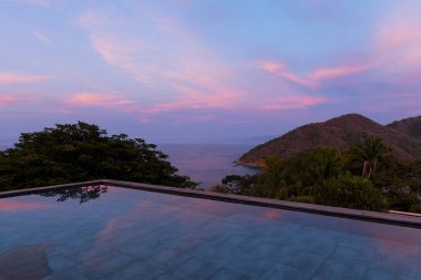 Swimming pool at sunset overlooking tropical rainforest and the bay of Puerto Vallarta, Jalisco, Mexico clipart