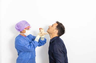 Koruyucu kıyafetli bir doktor olası bir koronavirüs enfeksiyonu için kişinin burnundan örnek alıyor.