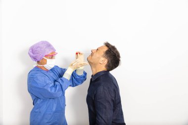 Koruyucu kıyafetli bir doktor olası bir koronavirüs enfeksiyonu için kişinin burnundan örnek alıyor.