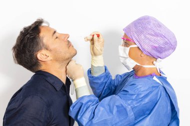 Koruyucu kıyafetli bir doktor olası bir koronavirüs enfeksiyonu için kişinin burnundan örnek alıyor.